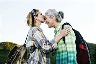 Caucasian daughter kissing mother on rural hilltop