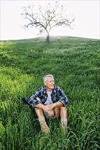 Older Caucasian man sitting on grassy hillside