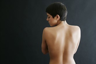 Rear view of nude Hispanic woman with tattoo on neck