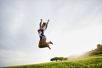 Black woman jumping for joy in field