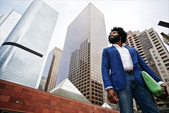 Mixed race businessman walking under skyscrapers