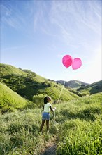Black girl with balloons on rural hillside