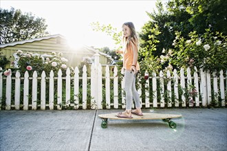 Caucasian girl riding skateboard on sidewalk
