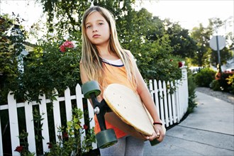 Caucasian girl holding skateboard on sidewalk