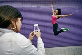 Woman photographing friend jumping for joy