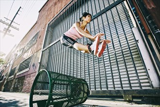 Mixed race woman jumping over trash can