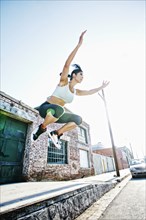 Mixed race woman jumping off sidewalk