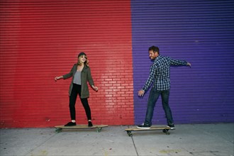 Caucasian couple riding skateboards on sidewalk