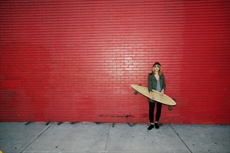 Caucasian woman holding skateboard on sidewalk