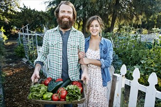 Couple standing with basket of vegetables in garden