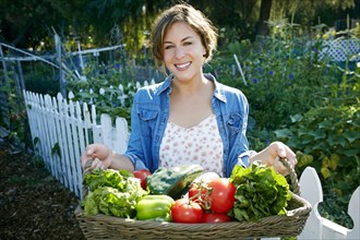 Mixed race woman holding basket of vegetables in garden