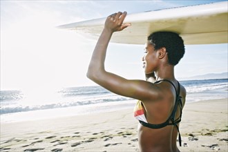 Black woman balancing surfboard on head at beach