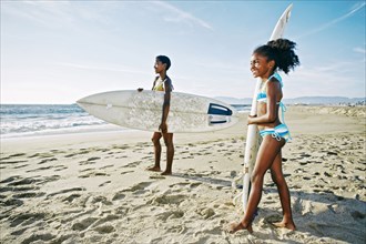 Black mother and daughter carrying surfboards on beach