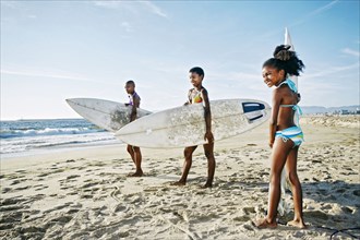 Three generations of Black women carrying surfboards on beach