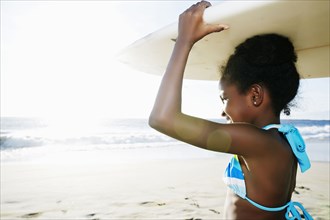 Black girl carrying surfboard on beach