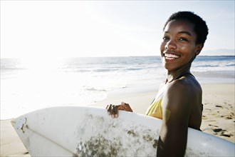 Black woman carrying surfboard on beach