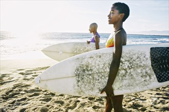 Black women carrying surfboards on beach