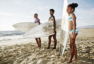 Three generations of Black women carrying surfboard on beach