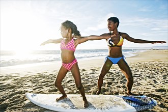 Black mother teaching daughter to surf on beach