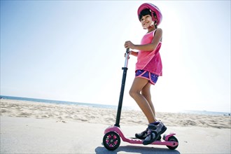 Mixed race girl riding scooter at beach