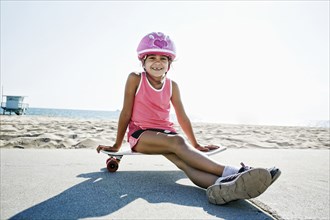 Mixed race girl sitting on skateboard at beach