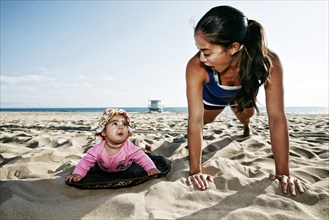 Mother and daughter doing push-ups at beach