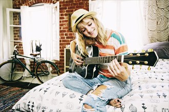 Caucasian woman playing guitar in bedroom