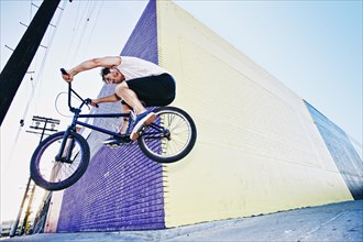 Caucasian man jumping on BMX bike on sidewalk