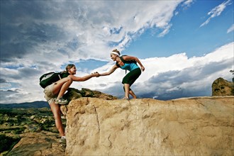 Woman helping friend climb rock formation
