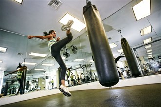 Mixed race woman kicking punching bag in gymnasium