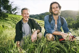 Caucasian hikers crouching in grass on mountain