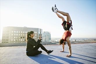 Woman photographing man doing handstand on urban rooftop