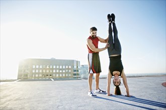 Caucasian man helping woman do handstand on urban rooftop