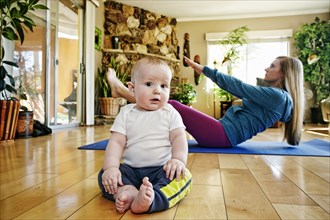Baby posing on floor while mother exercises