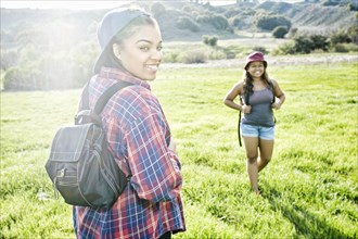 Smiling Mixed Race sisters backpacking in field near mountain