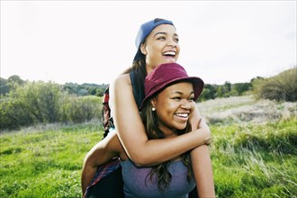 Mixed Race teenager giving sister piggyback ride in field