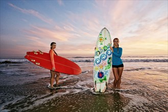 Women standing in ocean waves holding surfboards at beach