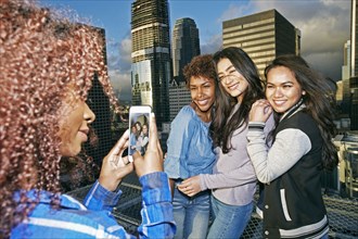 Stylish woman photographing friends on urban rooftop with cell phone