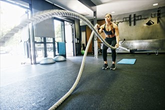 Mixed Race woman working out with heavy ropes in gymnasium