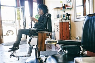Smiling Black hairdresser texting on cell phone in hair salon