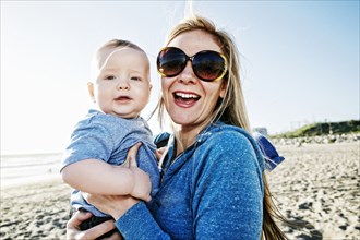 Smiling mother holding baby son at beach