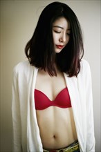 Smiling Asian woman standing at wall wearing red bra