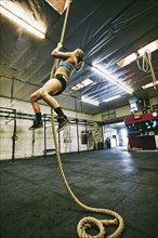 Caucasian woman climbing rope in gymnasium