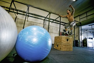 Caucasian man jumping on wooden crate in gymnasium