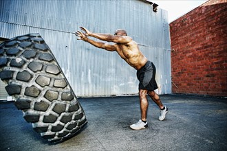 Black man working out with heavy tire outdoors
