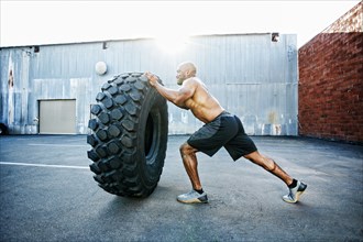 Black man working out with heavy tire outdoors