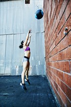 Jumping Caucasian woman throwing heavy ball at brick wall