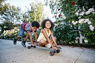 Mixed Race boy pushing sister on skateboard on sidewalk
