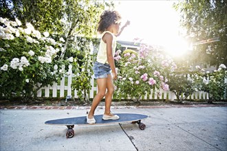 Mixed Race girl skateboarding on sidewalk