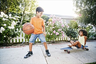 Mixed Race girl on skateboard watching brother dribbling basketball